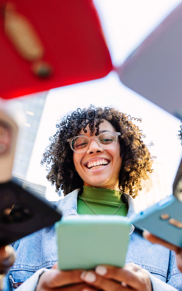 Happy young woman using mobile phones standing with friends outdoors.